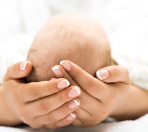 Mains manucurées tenant la tête d'un bébé