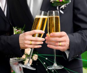 Mains de mariés gays avec alliances aux doigts et coupes de champagne à la main